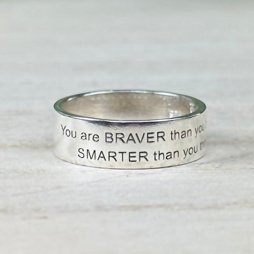 A Sterling Silver band ring with an engraved message on it, displayed against a wooden background.